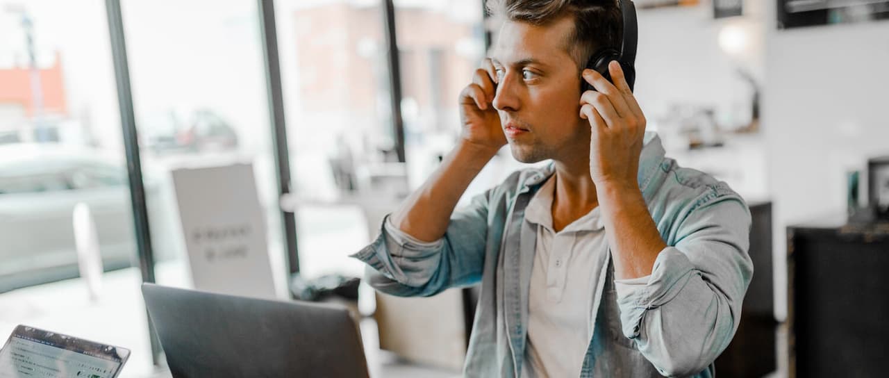 Ein junger Mann sitzt in einem hellen Raum vor einem aufgeklappten Laptop und greift sich mit beiden Händen an die Kopfhörer. Der Aufbau eines Lean Selling Konzepts braucht Zeit und Geduld, damit die Kundenzufriedenheit nicht leidet. Erfahre mehr dazu in unserem Beitrag!