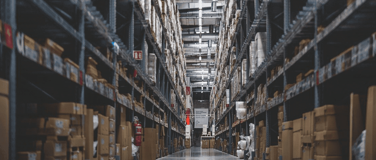 Blick in einen Gang einer Lagerhalle mit Hochregalen in denen jede Menge Pakete lagern. Wer Waren- und Informationsfluss synchronisiert, kommt dem optimalen Warenfluss sehr nahe!