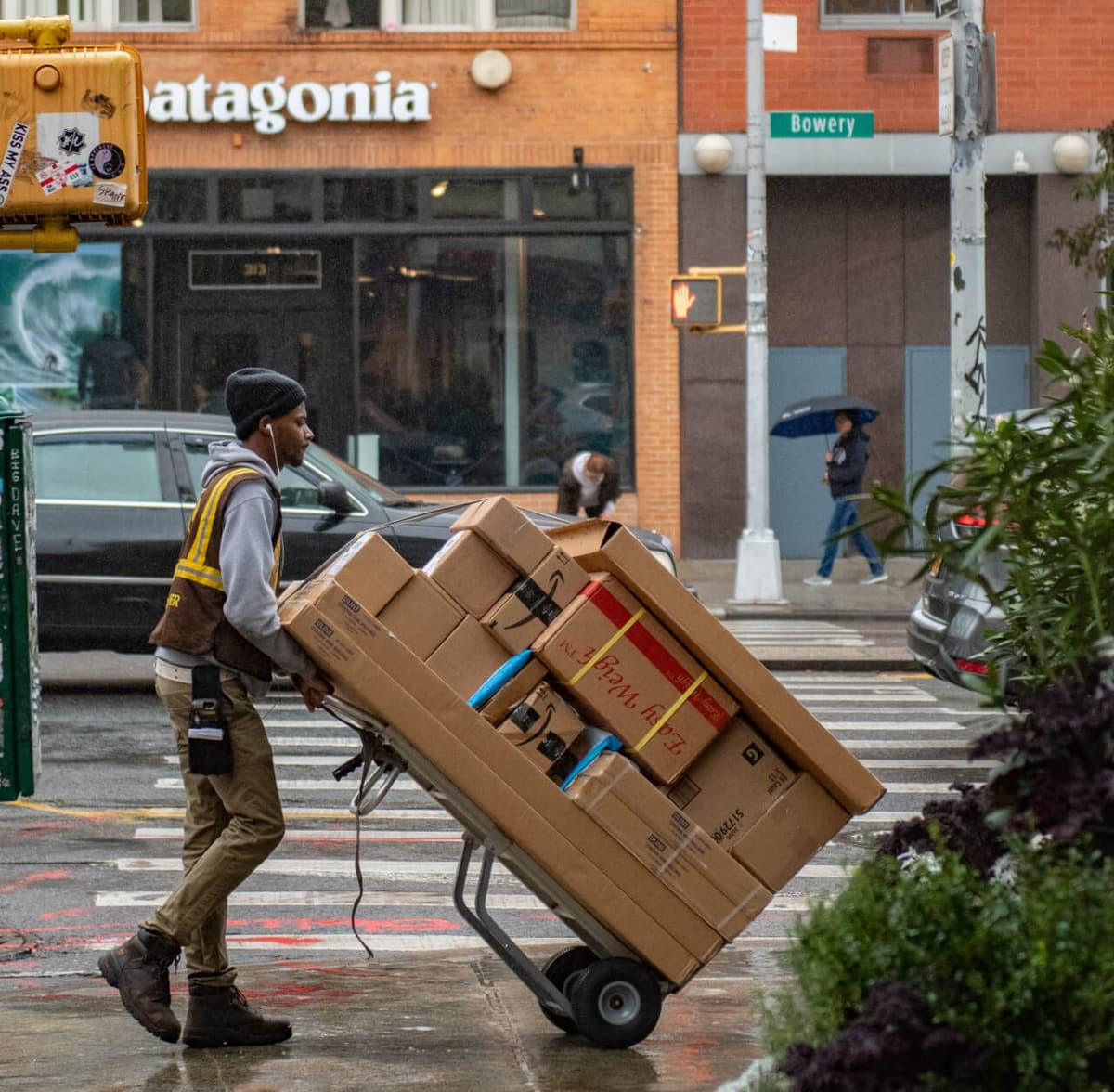 Blick auf eine Straßenkreuzung auf der ein Paketbote eine große Ladung Pakete auf einem Karren transportiert. Ein Retourenportal kann dir als Händler Mehraufwand abnehmen und deine Kund:innen binden. 