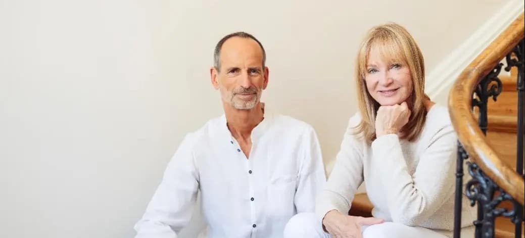 Roland Liebscher-Bracht und Petra Bracht sitzen auf einer Treppe, gekleidet in Weiß.