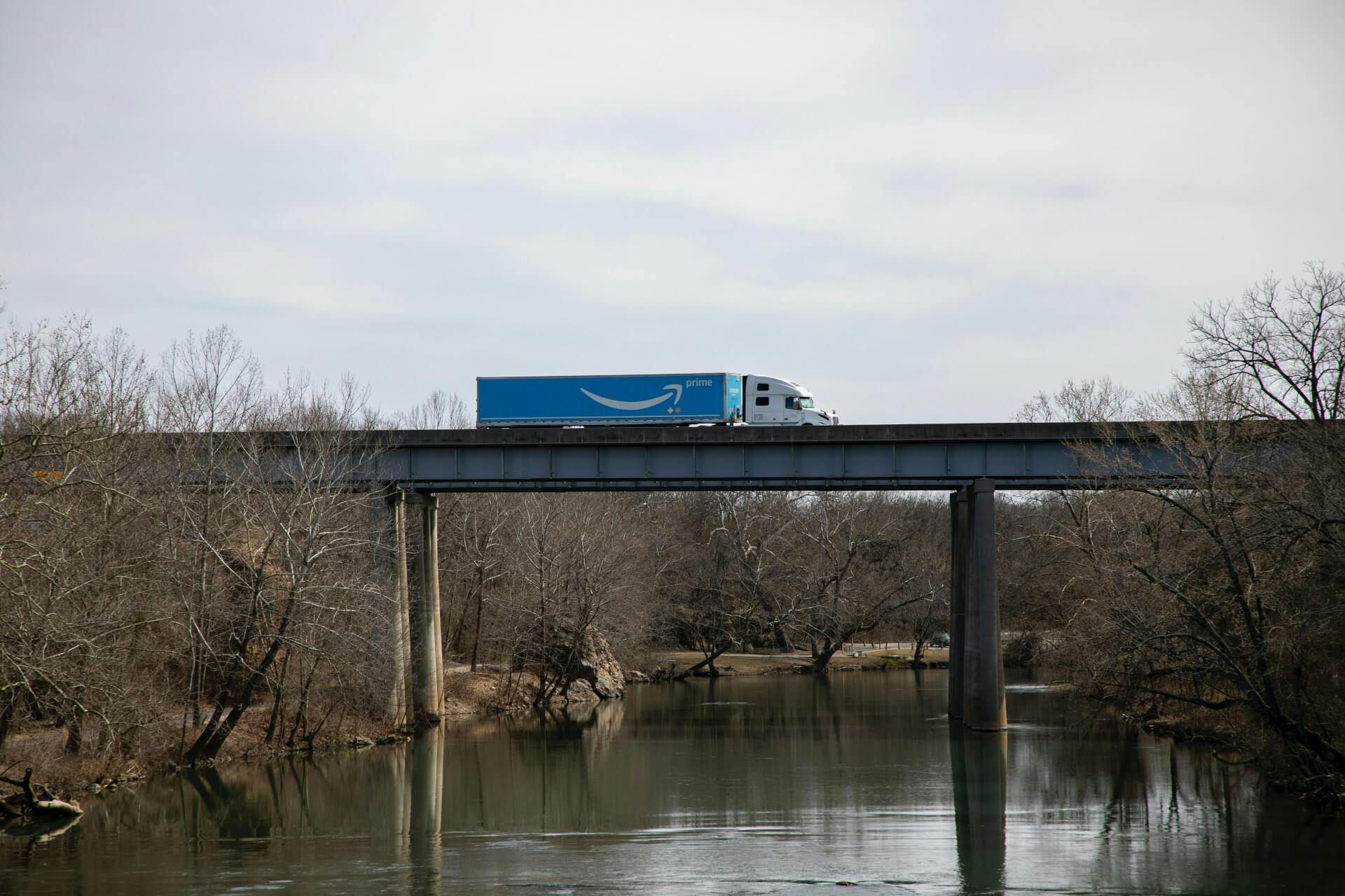 Blick auf eine Brücke über einem Fluss auf der ein Amazon Prime Truck fährt. Mit Prime by Seller wickelst du den Prime Versand aus deinem eigenen Lager ab. Auf was du dabei achten solltest, erfährst du in diesem Beitrag!