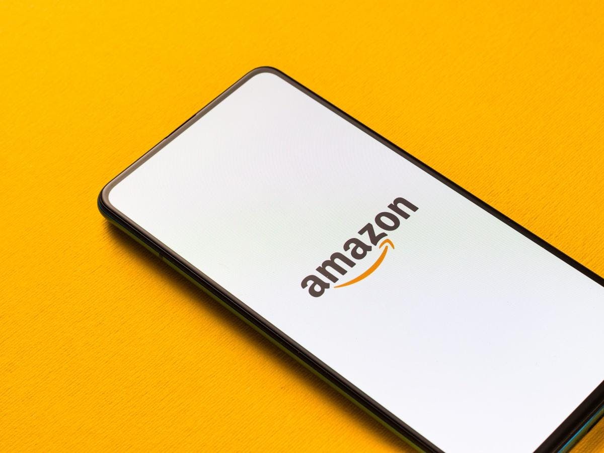 Ein Handy, welches das Amazon-Logo zeigt, liegt auf gelben Hintergrund