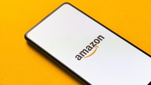 Ein Handy, welches das Amazon-Logo zeigt, liegt auf gelben Hintergrund